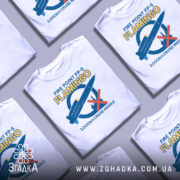 Футболка фламінго крилата ракета білого кольору, зображена на манекені з правого боку, фон світло-сірий, принт містить синю ракету та червоний хрест, текст на футболці жовтого та синього кольорів.