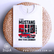 Футболка Ford Mustang класика, біла, складена на плетеній кошику, фон світло-сірий, принт з червоним автомобілем Ford Mustang 1964, логотипом Ford, написом 'BUILT TO BE LEGENDARY'.