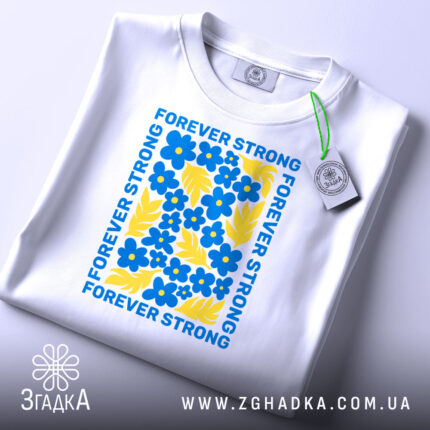 Футболка forever strong, білого кольору, складена на поверхні, фон світлий, принт з яскравими синіми квітами та жовтими листками, текст 'FOREVER STRONG' розташований по периметру, на футболці є етикетка з зеленим шнурком.