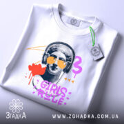 Футболка Girls Rule Art білого кольору, складена на поверхні, зображена з верхнього ракурсу, фон світло-сірий, принт з графічним зображенням статуї з навушниками та сонцезахисними окулярами, кольори принта: червоний, фіолетовий, жовтий, чорний, на футболці є етикетка.