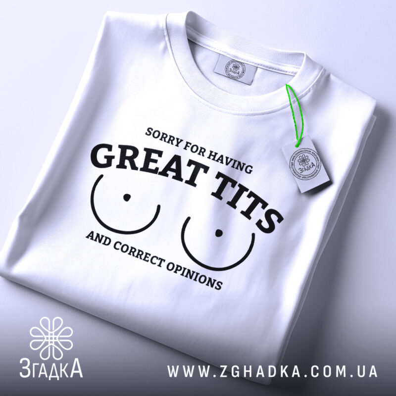 Футболка great tits білого кольору, складена на столі, ракурс зверху, фон світло-сірий, принт чорного кольору з текстом 'SORRY FOR HAVING GREAT TITS AND CORRECT OPINIONS' і малюнком двох грудей, на футболці є зелений ярлик.