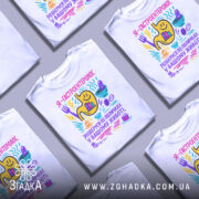 Футболка гастроентеролог, білого кольору, зображена на манекені з ближнього ракурсу, фон світло-сірий, принт кольоровий з жовтим шлунком, смайликами та предметами, що символізують гастрономію.