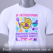 Футболка гастроентеролог, білого кольору, зображена з верхнього ракурсу, фон світло-сірий, принт кольоровий з жовтим шлунком, смайликами та предметами, що символізують гастрономію, з етикеткою на комірці.