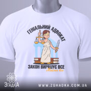 Футболка геніальний адвокат, біла, складена на столі, фон світло-сірий, принт з адвокатом у білому одязі, що тримає ваги та меч, текст чорний і жовтий, на комірці видно етикетку.