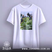 Футболка геть з України, біла, підвішена на вішалці, фон світлий, принт зображує жінку та істоту на городі, текст на принті: 'Геть з України, москаль некрасивий!'