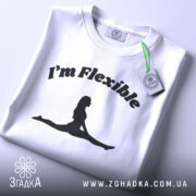 Футболка гнучка йога силует, біла, складена на столі, фон світло-сірий, принт чорний з написом 'I'm Flexible' та силуетом жінки в позі розтяжки, з етикеткою на зеленій стрічці.