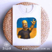 Футболка гомер з тризубом, біла, складена на плетеній кошику, фон світло-сірий, принт з гомером у чорній футболці з тризубом на жовто-блакитному фоні.