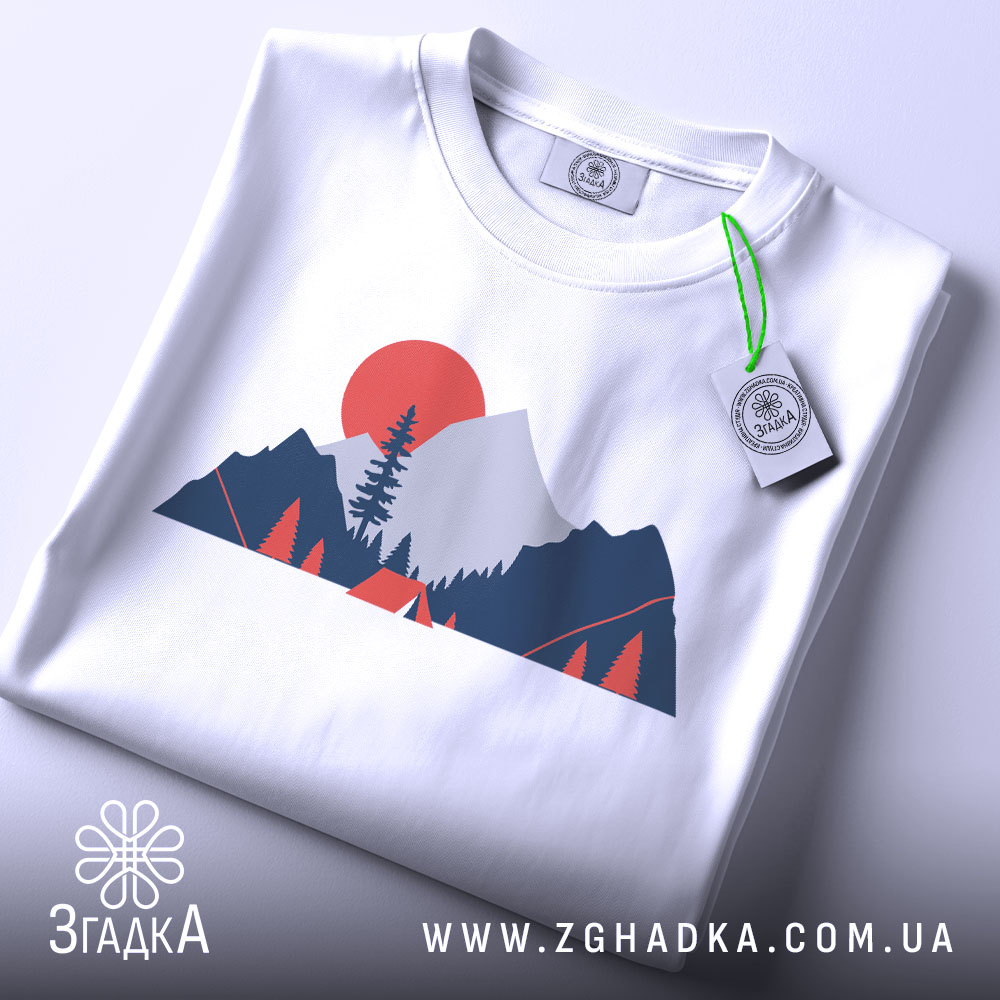 Футболка гори кемпінг, біла, складена на столі, фон світлий, принт з горами, деревом та сонцем у червоному кольорі, з етикеткою.