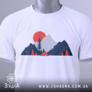 Футболка гори кемпінг, біла, складена на столі, фон світлий, принт з горами, деревом та сонцем у червоному кольорі, з етикеткою.