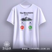 Футболка гори на зв’язку, біла, підвішена на вішалці, фон світло-сірий, принт з горами, текстом 'The Mountains Mobile' та іконками дзвінка.