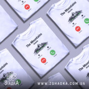 Футболка гори на зв’язку, біла, зображена на манекені з правого боку, фон світло-сірий, принт з горами, текстом 'The Mountains Mobile' та іконками дзвінка.
