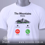 Футболка гори на зв’язку, біла, складена на столі, фон світло-сірий, принт з горами, текстом 'The Mountains Mobile' та іконками дзвінка, з зеленим ярликом.