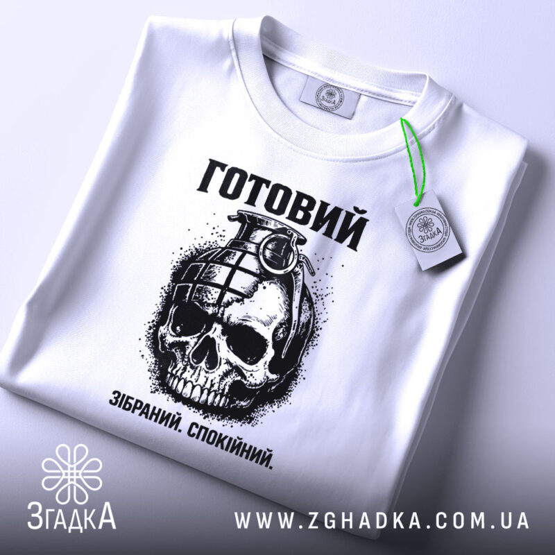 Футболка готовий до дій, біла, зображена зверху, на ній підвішений етикет, фон світло-сірий, принт з черепом та гранатою, текст "Готовий. Зібраний. Спокійний." під малюнком.