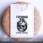 Футболка готовий до дій, біла, зображена зверху на плетеній кошику, фон білий, принт з черепом та гранатою, текст "Готовий. Зібраний. Спокійний." під малюнком.