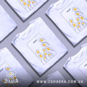 Футболка гуси гумор, біла, зображена на манекені, фон світло-сірий, принт з жовтими гусячими головами та текстом 'what?' у верхній частині.