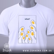 Футболка гуси гумор, біла, складена на поверхні, фон світло-сірий, принт з жовтими гусячими головами та текстом 'what?' у верхній частині, з зеленим ярликом.