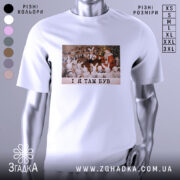 Футболка і я там був. Біла футболка з принтом, на якому зображена сцена з дітьми у костюмах зайців, що сидять навколо Діда Мороза. Принт кольоровий, на фоні святкова ялинка. Текст на принті чорний: 'I Я ТАМ БУВ'.