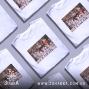 Футболка і я там був. Біла футболка з принтом, на якому зображена сцена з дітьми у костюмах зайців, що сидять навколо Діда Мороза. Принт кольоровий, на фоні святкова ялинка. Текст на принті чорний: 'I Я ТАМ БУВ'.