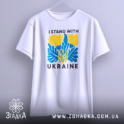Футболка I Stand Ukraine білого кольору, підвішена на вішалці, фон світло-сірий, принт з жовтими квітами та синіми елементами, а також напис 'UKRAINE'.