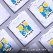 Футболка I Stand Ukraine білого кольору, зображена з фронтального ракурсу на манекені, фон світло-сірий, принт містить жовті квіти та сині елементи, а також тризуб та напис 'UKRAINE'.
