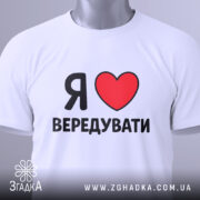 Футболка я люблю вередувати, біла, складена на плоскій поверхні, фон світлий, принт з червоним сердечком і чорним текстом, на комірці є етикетка.