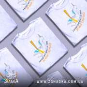Футболка я не буду простішою. Біла футболка на манекені, з принтом у вигляді єдинорога, що тримає жовті стрічки. Принт кольоровий, з блакитним волоссям єдинорога та текстом українською мовою.