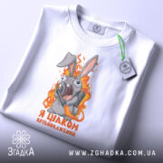 Футболка я цілком врівноважений, білого кольору, складена на столі, фон світло-сірий, принт з кроликом, який виглядає емоційно, тримаючи гранату, текст на футболці чорного кольору, з зеленим ярликом.