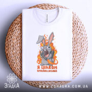 Футболка я цілком врівноважений, білого кольору, складена на плетеному кошику, фон білий, принт з кроликом, який тримає гранату, оточений полум'ям, текст на футболці чорного кольору.