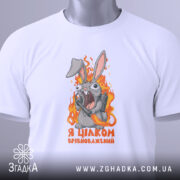 Футболка я цілком врівноважений, білого кольору, складена на столі, фон світло-сірий, принт з кроликом, який виглядає емоційно, тримаючи гранату, текст на футболці чорного кольору, з зеленим ярликом.