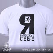 Футболка я виходжу з себе. Біла футболка складена, з чорним принтом, зображення чоловіка, що біжить, видно чітко. На футболці є етикетка з зеленим шнурком. Фон світло-сірий.