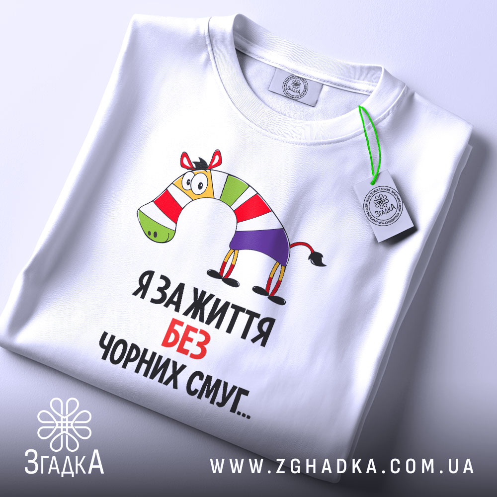 Футболка я за життя, білого кольору, складена на поверхні, фон світло-сірий, принт з зеброю в смугастому одязі та написом "Я за життя без чорних смуг...", на комірці видна етикетка.