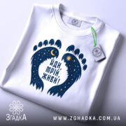 Футболка йди мрій живи, біла, зображена зверху, фон світло-сірий, принт у вигляді слідів з зірками та місяцем, на комірці є етикетка.