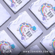 Футболка єдинороги білого кольору, зображена з правого ракурсу на манекені, фон світло-сірий, принт з веселкою та єдинорогами, текст "ЧАРІВНА НА ВСЮ ГОЛОВУ" в чорному кольорі.