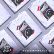 Футболка єнот гумор НЛО білого кольору, зображена в анфас на манекені, фон нейтральний, принт містить зображення єнота з усмішкою, над ним літаюча тарілка, червона смужка та текст "А я казав!".