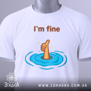 Футболка I'm fine білого кольору, зображена з верхнього ракурсу, складена на поверхні, фон світло-сірий, принт з рукою, що піднімає великий палець, оточений блакитними хвилями, з етикеткою на зеленому шнурку.