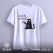 Футболка їсти чи не їсти. Біла футболка підвішена на вішалці, з принтом чорного кота, який тримає круасан. Фон світло-сірий, футболка має короткі рукави.