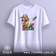 Футболка капібара білого кольору, підвішена на вішалці, з принтом капібари в кепці та золотому ланцюгу, фон світло-сірий.