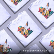 Футболка капібара білого кольору, зображена на манекені, з принтом капібари в кольоровій кепці та золотому ланцюгу, фон світло-сірий.