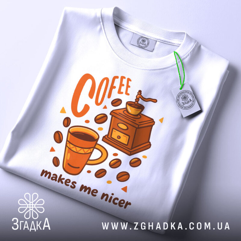 Футболка кавовий характер, біла, зображена зверху, фон світлий, принт з чашкою кави, кавомолкою та написом 'makes me nicer', з етикеткою на рукаві.