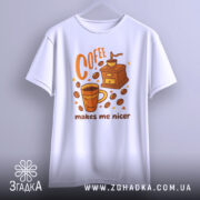 Футболка кавовий характер, біла, зображена на вішалці, фон світлий, принт з чашкою кави, кавомолкою та написом 'makes me nicer' у помаранчевих тонах.