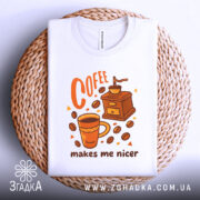 Футболка кавовий характер, біла, зображена зверху на плетеній основі, фон світлий, принт з чашкою кави, кавомолкою та написом 'makes me nicer' у помаранчевих тонах.