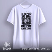 Футболка керую цим цирком, білого кольору, підвішена на вішалці, фон світло-сірий, принт з тигром у капелюсі та текстом "Я КЕРУЮ ЦИРКОМ!" у чорному кольорі.