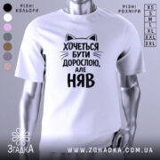 Футболка хочеться бути дорослою. Біла футболка з чорним принтом, зображена з фронтального ракурсу на манекені. Принт містить текст з котячими вушками, що говорить: 'Хочеться бути дорослою, але НЯВ'.