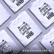 Футболка хочеться бути дорослою. Біла футболка з чорним принтом, зображена з фронтального ракурсу на манекені. Принт містить текст з котячими вушками, що говорить: 'Хочеться бути дорослою, але НЯВ'.