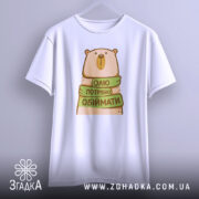 Футболка хочу обіймати, біла, зображена з фронтального ракурсу, фон світло-сірий, принт з ведмедем, який тримає зелену стрічку з написом 'Олі потрібно обіймати'.