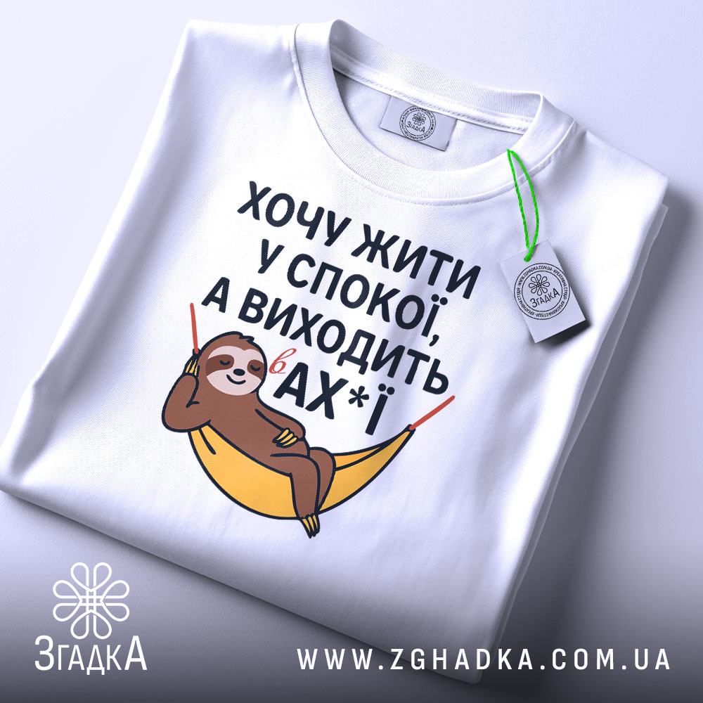 Футболка хочу жити спокійно, білого кольору, з верхнього ракурсу, на фоні світло-сірого градієнту, з принтом лінивця у гамаку, текст розташований по центру, з зеленим ярликом.