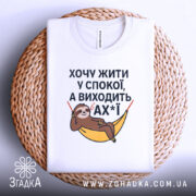 Футболка хочу жити спокійно, білого кольору, з верхнього ракурсу, на фоні плетеного кошика, з принтом лінивця у гамаку, текст розташований по центру.
