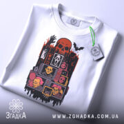 Футболка хорор білого кольору, складена на столі, фон світло-сірий, принт з черепом, чорними руками та жахливими персонажами, з зеленим ярликом.