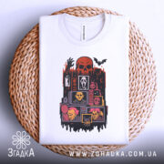 Футболка хорор білого кольору, складена на плетеному кошику, фон світло-сірий, принт з черепом, чорними руками та жахливими персонажами, виглядає акуратно.