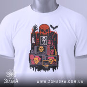 Футболка хорор білого кольору, складена на столі, фон світло-сірий, принт з черепом, чорними руками та жахливими персонажами, з зеленим ярликом.